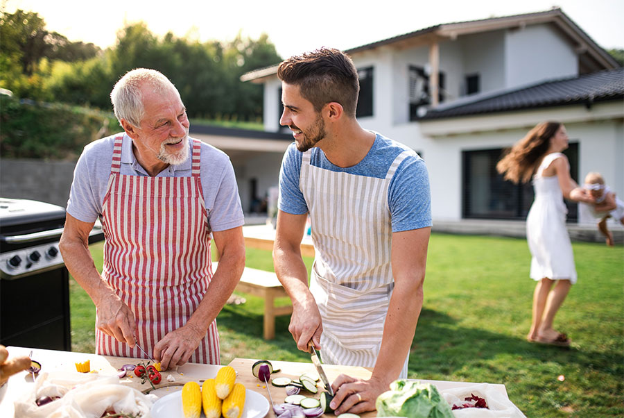 father and grown son in backyard smiling at each other and preparing to barbecue